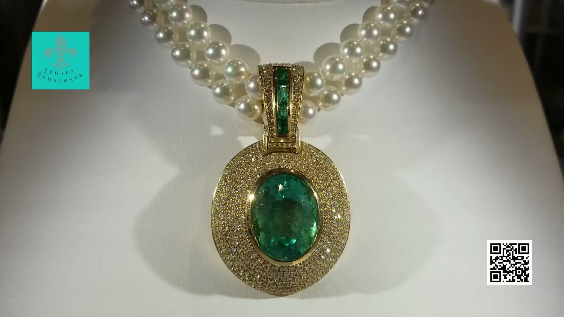 An emerald pendant surrounded by diamonds on a pearl necklace, displayed on a white stand with a logo and qr code in the background.