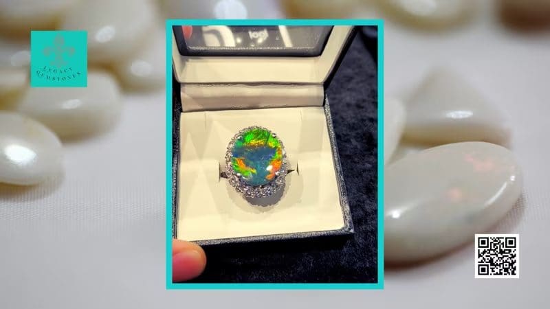 Opal ring in a box with brilliant play-of-color, displayed on a background of smooth stones, with a blurred qr code to the right.