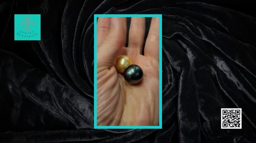 A hand holding two large pearls, one gold and one dark blue, resting on a black velvet background.