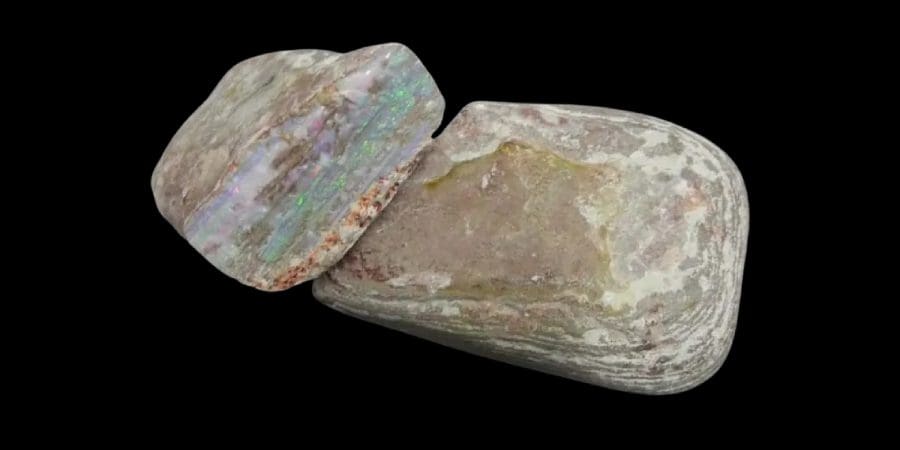 Two halves of an opal-filled geode on a black background, showing iridescent colors inside a rough, stone exterior.