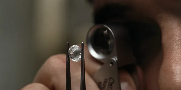 Close-up of a person examining a diamond with tweezers and a magnifying glass, focusing intently on its details.