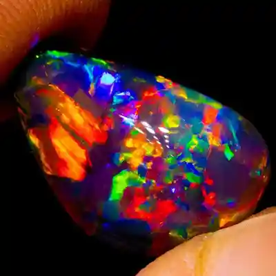 A vibrant, multicolored Australian Black opal held between fingers, displaying a vivid play of rainbow colors.