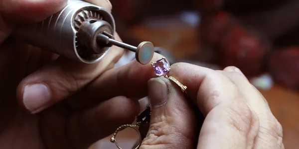 Close-up of a jeweler's hands using a rotary tool to polish a gemstone set in a ring.