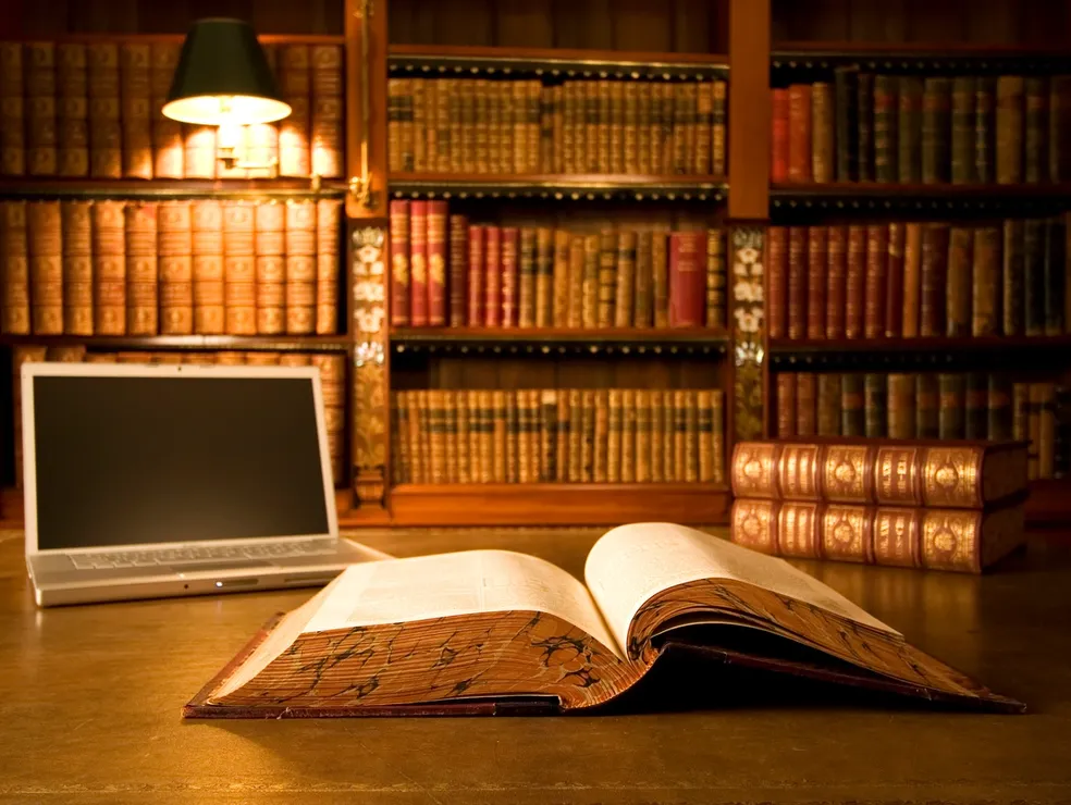 Library desk with open book and laptop, symbolizing knowledge and research in jewellery design and legacy gemstones.